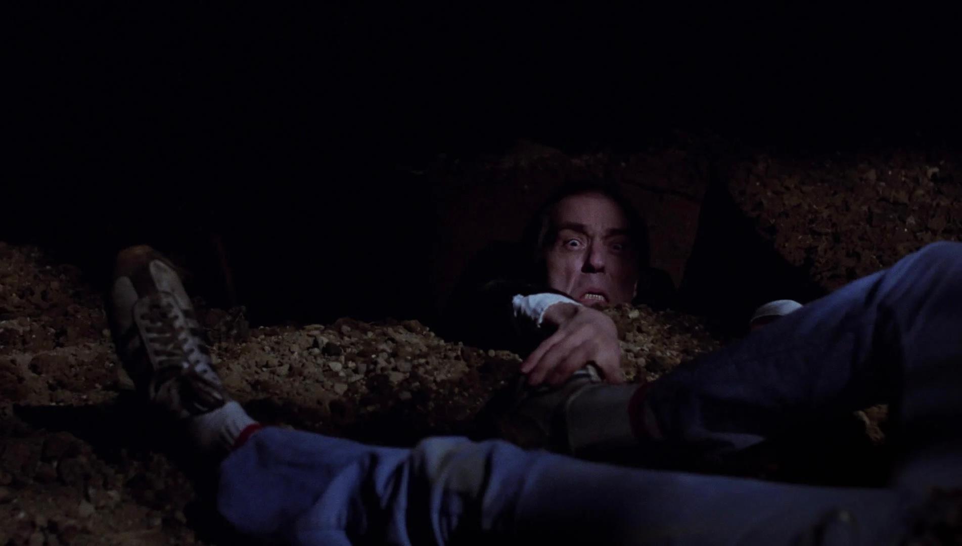 Phantasm-7 | film.org.pl Man emerging from a dark dirt hole at night, reaching with a terrified expression toward the edge of the pit.
