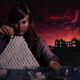 Woman stacks a pyramid of white sugar cubes at a table, with a looming red sky and a giant hand reaching from the clouds toward a distant haunted house.