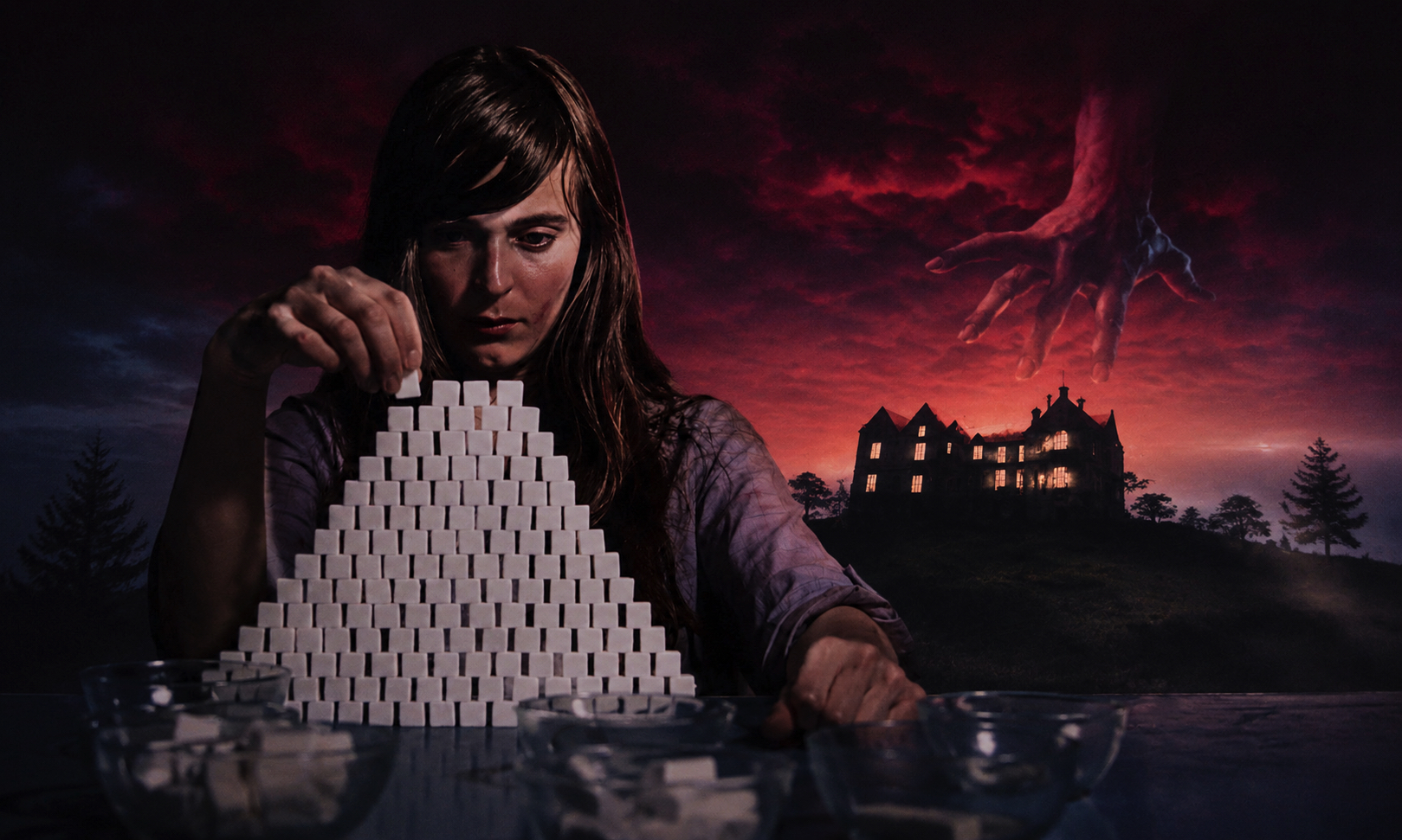 Woman stacks a pyramid of white sugar cubes at a table, with a looming red sky and a giant hand reaching from the clouds toward a distant haunted house.