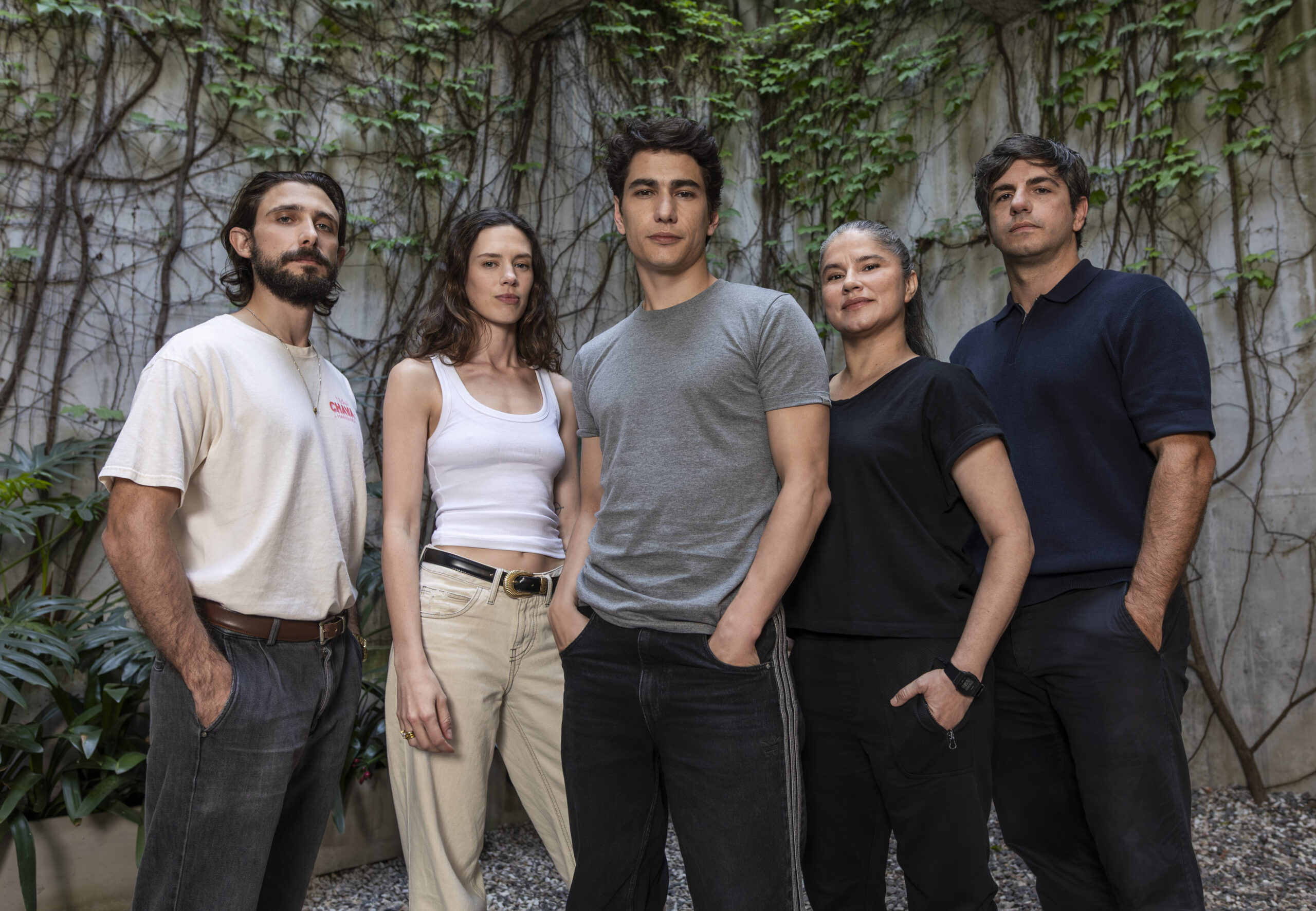 Five adults stand side by side outdoors in front of a wall covered with ivy, posing for a group photo.
