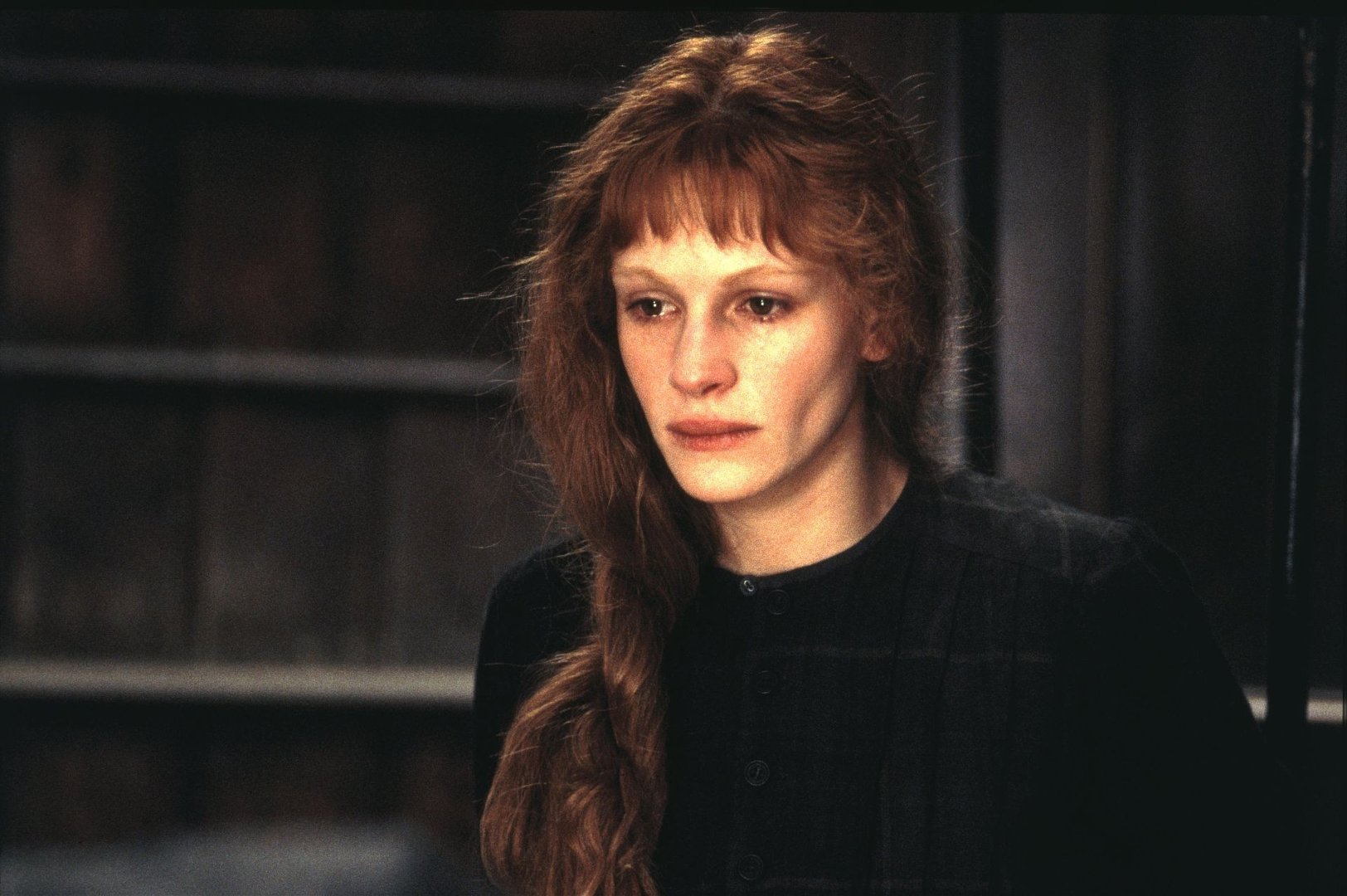 Mary-Reilly | film.org.pl Young woman with long red hair in a thick braid, wearing a black buttoned dress, looking somber in a dim interior.