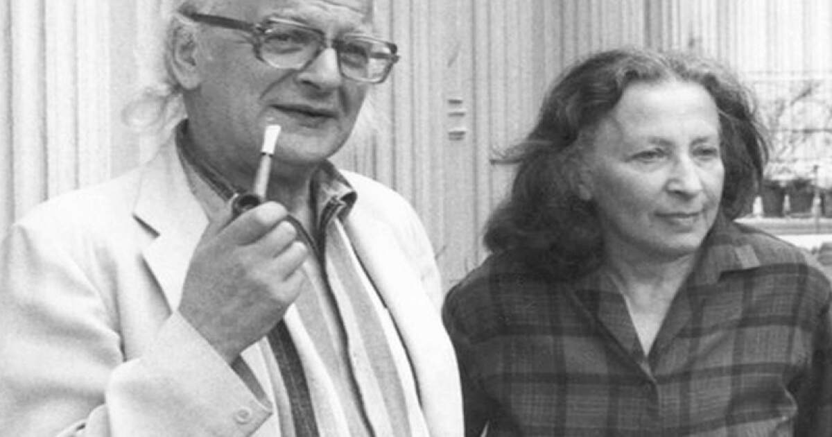 Moi-Themersonowie-2 | film.org.pl Older man with glasses and a pipe standing beside a woman in a plaid shirt outdoors, near a fence or railing.