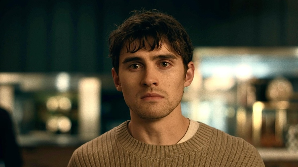 OBSESSION - Bear BEGINNING | film.org.pl Close-up portrait of a young man with brown hair wearing a beige knit sweater, looking at the camera in a softly lit room.