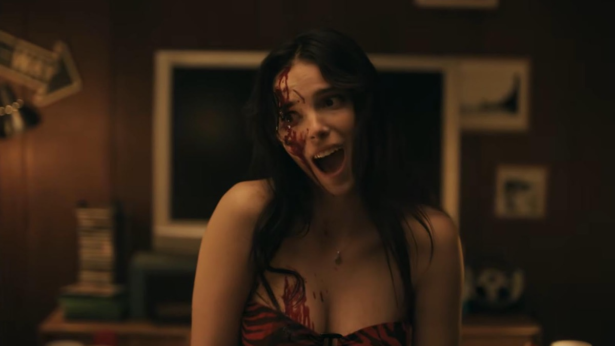 Woman with blood on her face and chest, screaming in a dimly lit room, conveying horror.