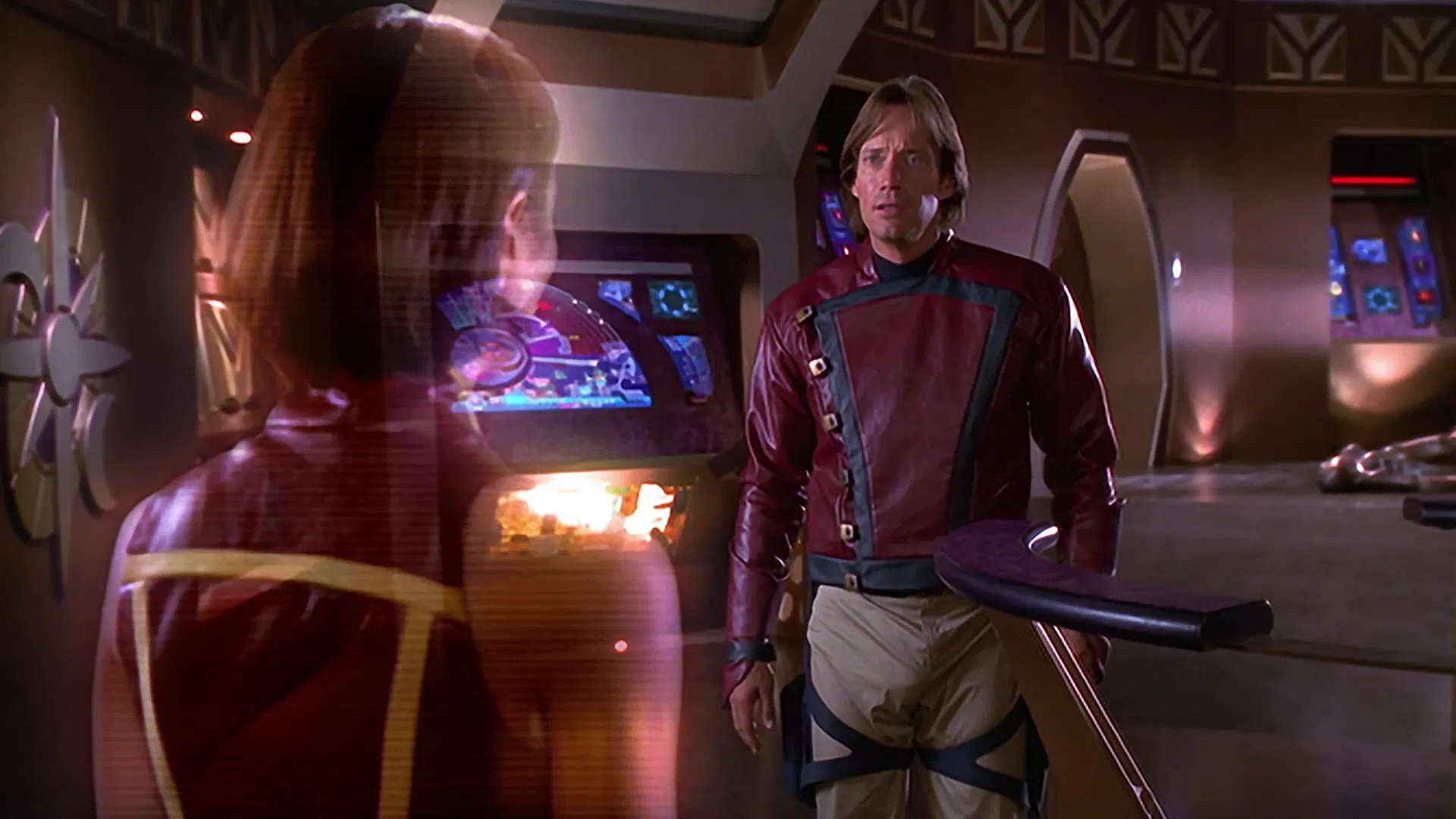 Man in a red Starfleet-style uniform confronts a translucent holographic woman in a high-tech ship corridor with glowing screens behind them.