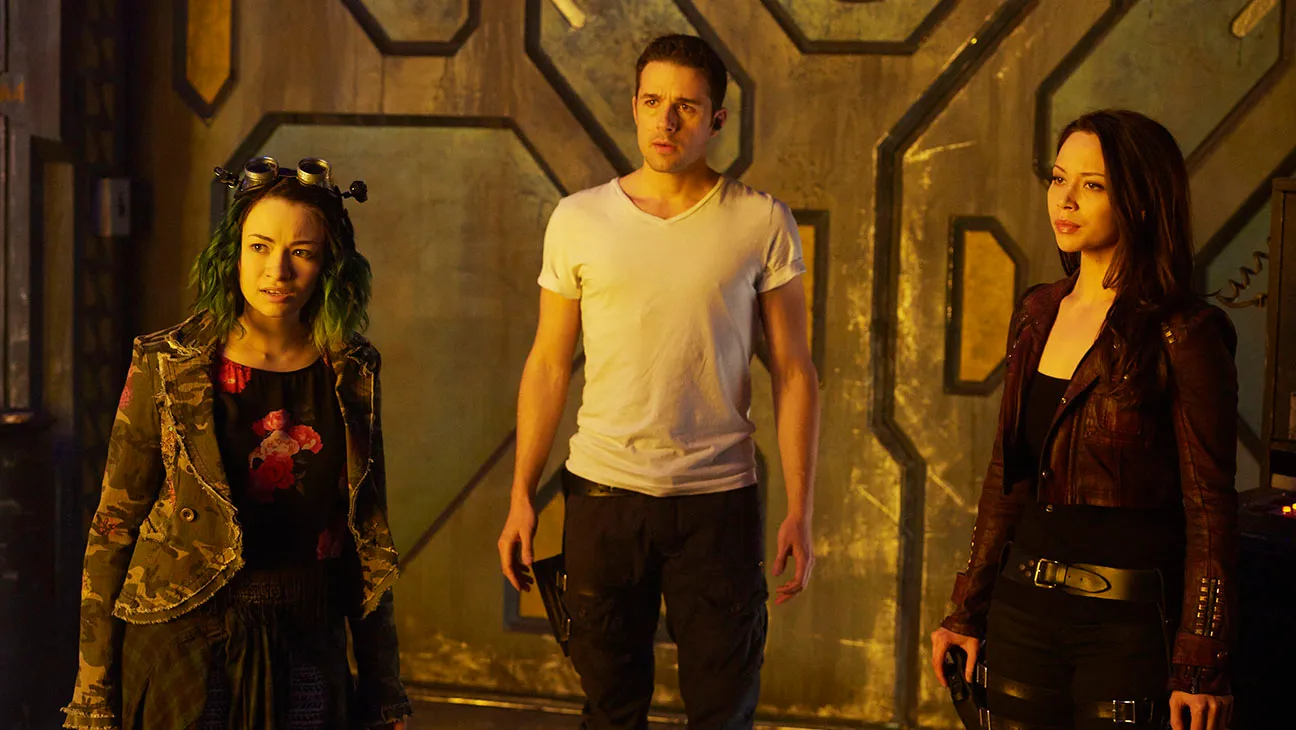 dark-matter-3 | film.org.pl Three people stand in a dim, industrial set with metallic walls, looking tense or worried.