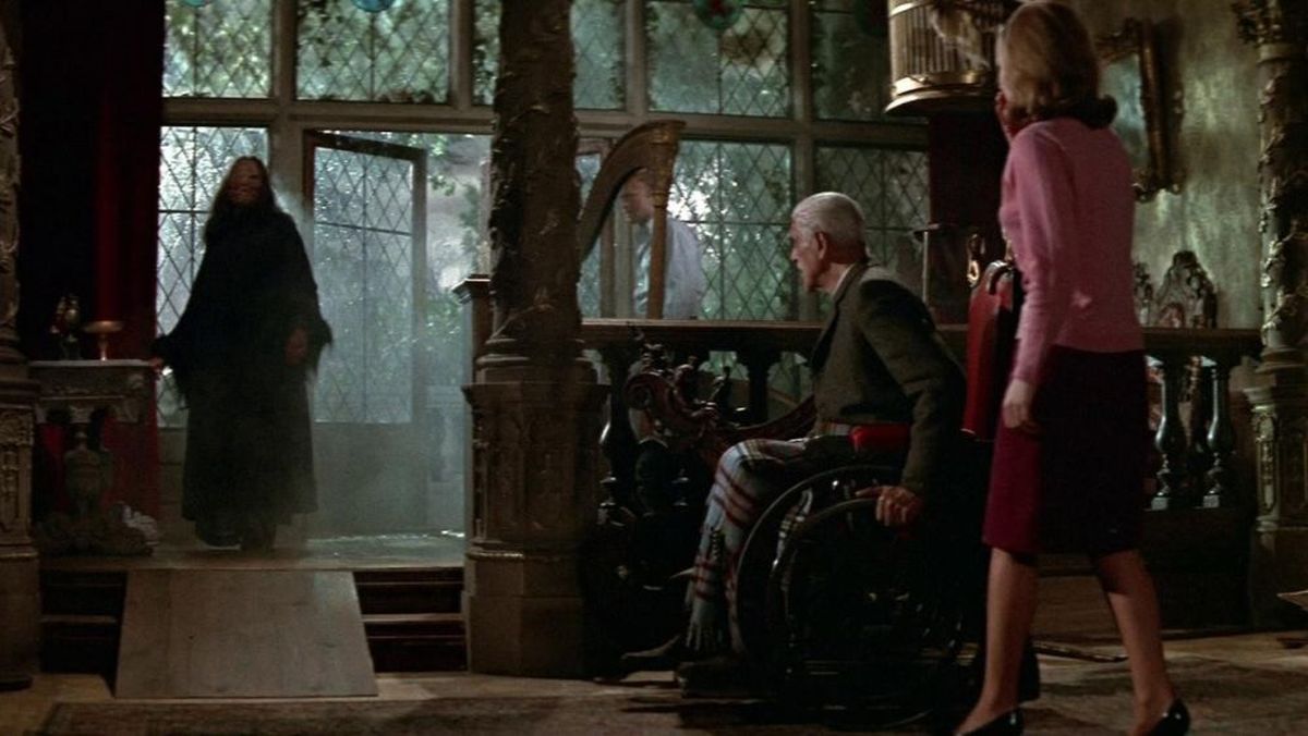 Man in a wheelchair and a woman in a pink jacket face a shadowy figure entering a dim, ornate room through a doorway.