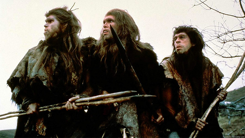 Three rugged men in fur garments with wooden spears stand outdoors, looking toward something off-camera.