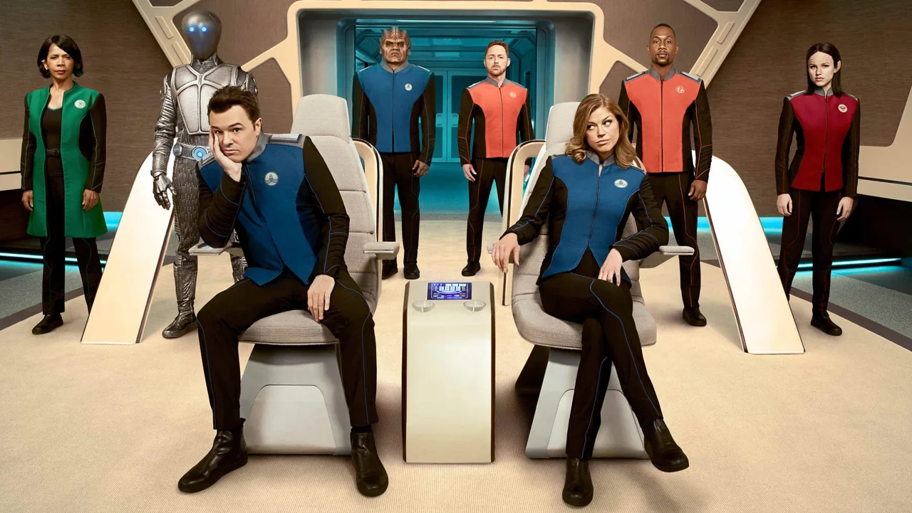 orville-2 | film.org.pl Crew in futuristic uniforms on a starship bridge, with two seated in the foreground and several officers standing behind; ready for launch.