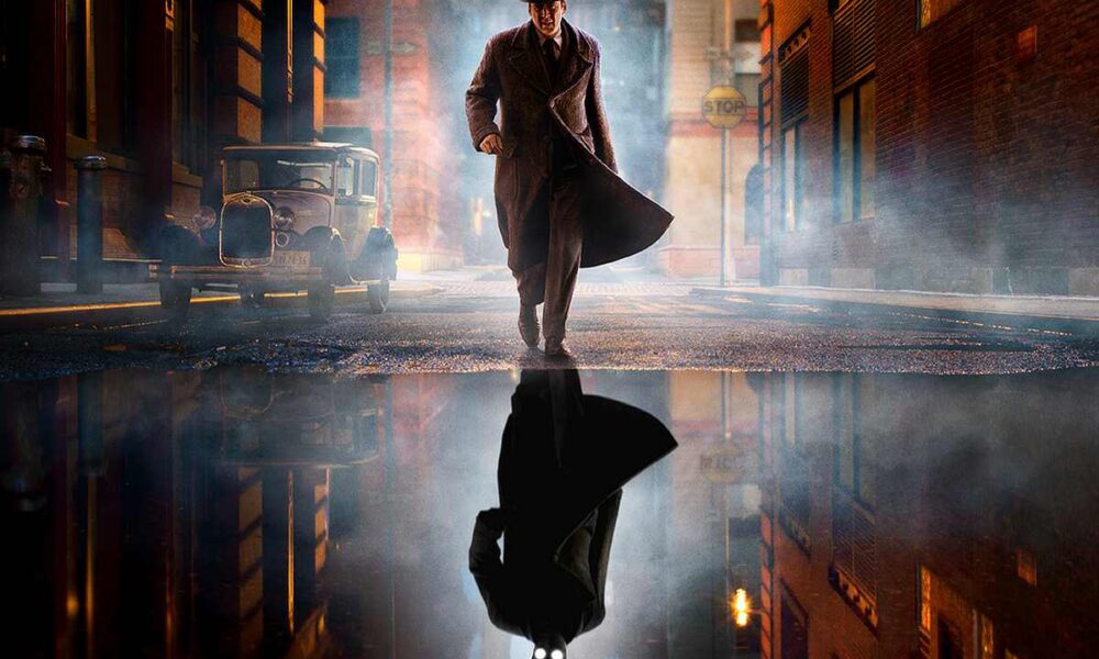 Noir-styled man in a long trench coat and fedora walks down a foggy city street at night, his reflection visible in a puddle.