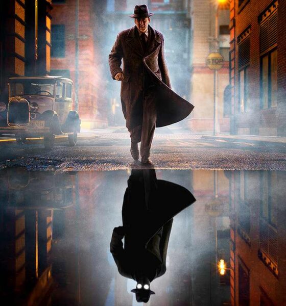 Noir-styled man in a long trench coat and fedora walks down a foggy city street at night, his reflection visible in a puddle.