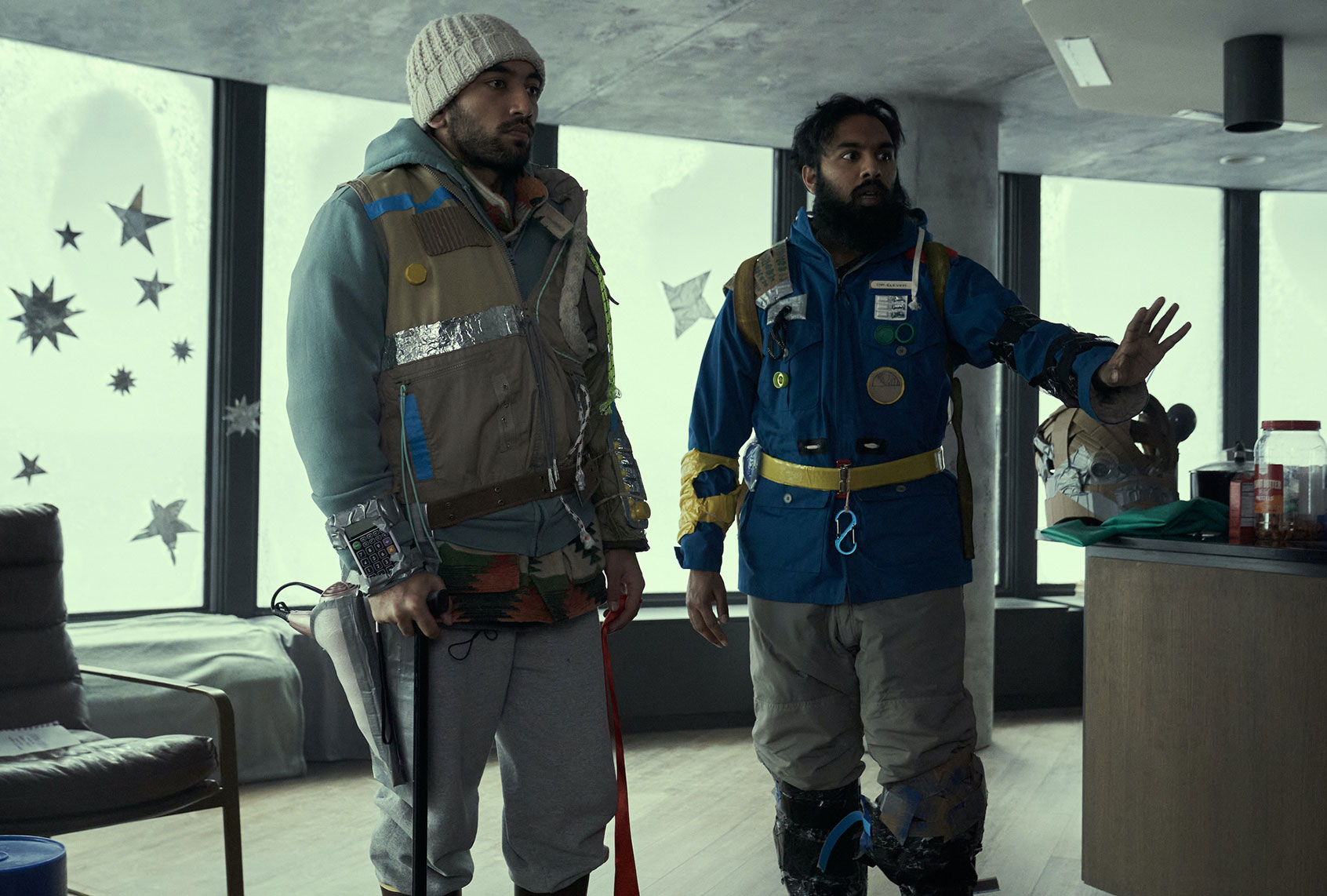 Two climbers in a modern living room wearing mountaineering gear, one with an ice axe.”,