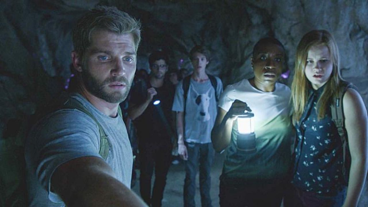 under-the-dome | film.org.pl Group of hikers in a dark cave; man in foreground takes a selfie while others shine a lantern behind him.
