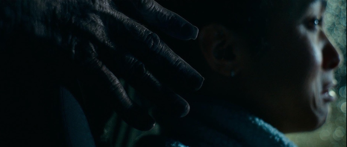 Close-up of a person in a car at night, a gloved hand resting on their shoulder from behind.
