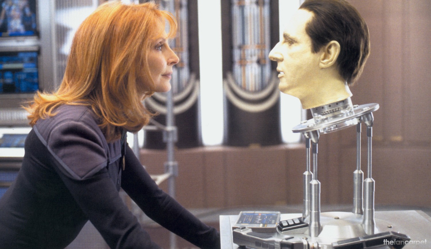 Star-Trek-Nemesis | film.org.pl Woman in a dark outfit leans toward a life-size humanoid head mounted on a metal stand in a high-tech lab.
