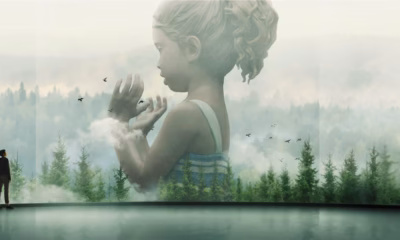 Man standing in a gallery viewing a large double-exposure mural: a girl’s semi-transparent profile blending into a forest landscape.