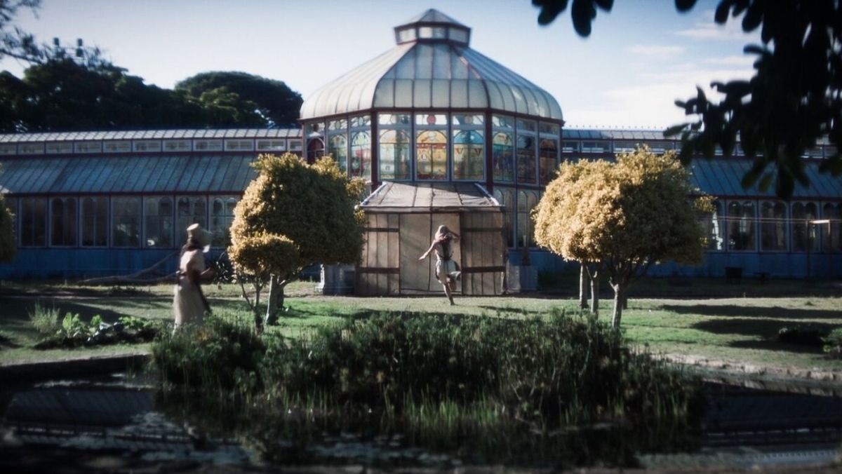 glasshouse 2 | film.org.pl Glass-domed conservatory in a lush garden, with a small pond in the foreground and two people nearby.