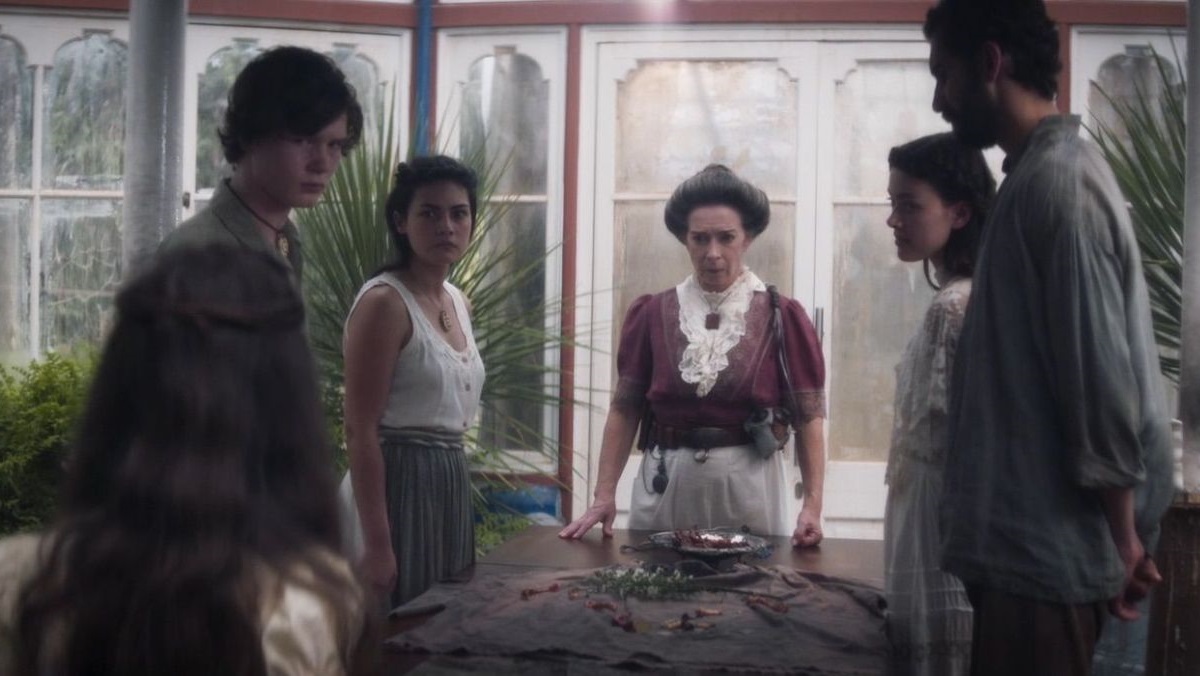 glasshouse 5 | film.org.pl Six people in period costume stand around a table in a glass conservatory, looking tense at the centerpiece dish.