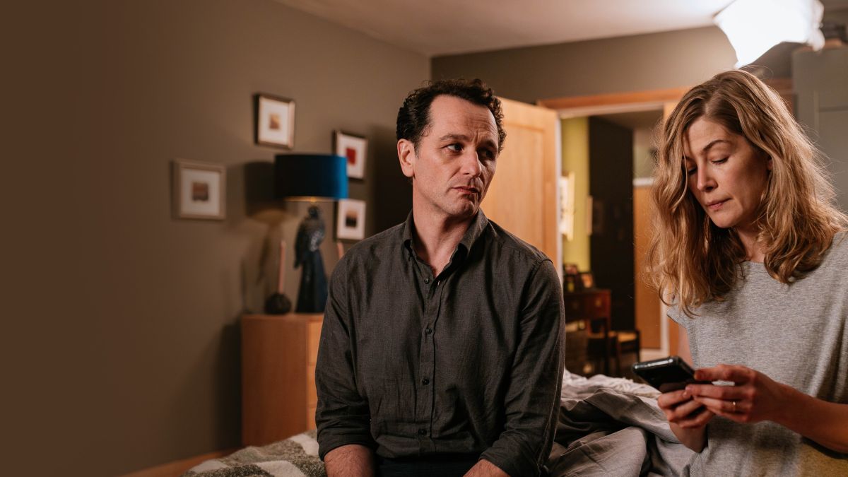 hallowroad 2 | film.org.pl Man and woman sit on a bed in a dimly lit bedroom; the woman holds a smartphone while the man looks away thoughtfully.