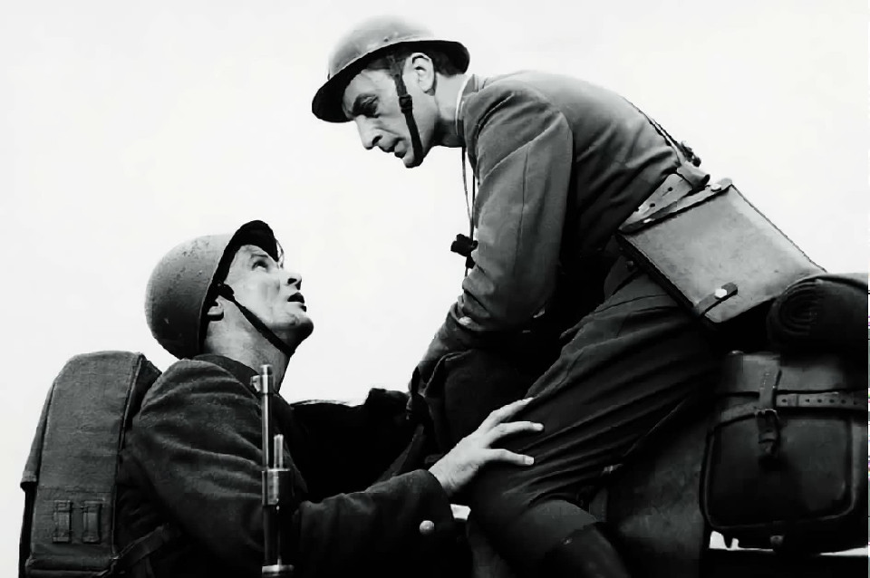 Black-and-white photo of a World War II soldier helping another climb onto a horse, both wearing helmets and gear.
