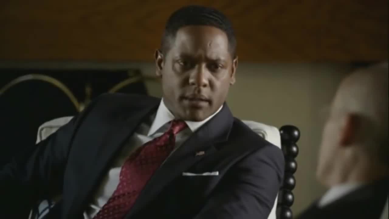 the-event | film.org.pl Man in a dark suit and red tie sits in a chair, looking toward someone off-screen as he talks in a formal setting.