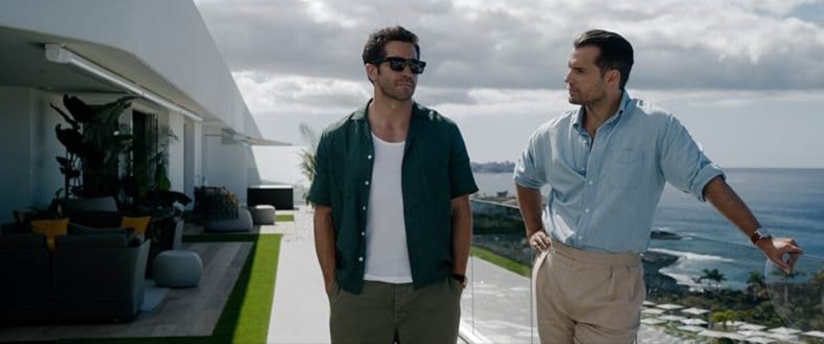 zawodowcy-zdjęcie-główne | film.org.pl Two men stand on a sunny terrace overlooking the ocean, dressed casually in short sleeves and chinos, chatting by a glass railing.