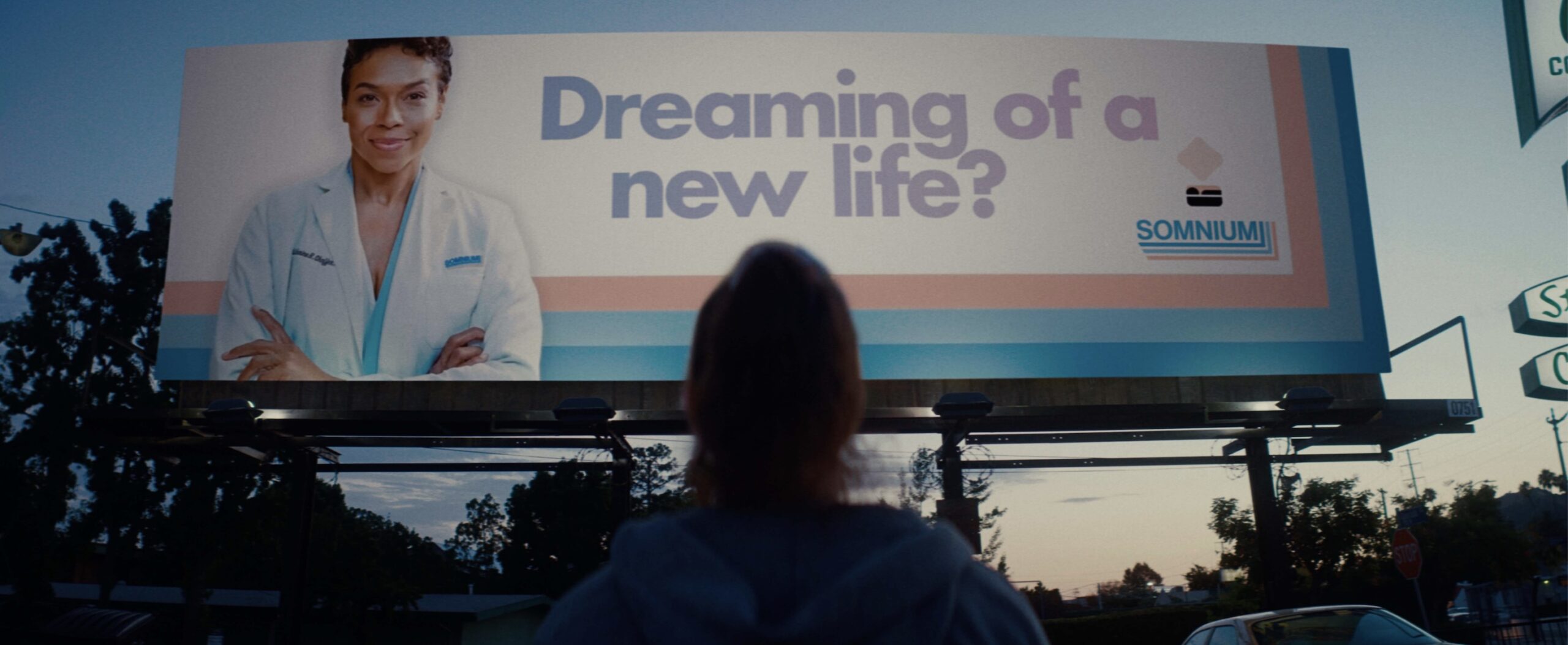 Screenshot | film.org.pl Person standing in front of a large outdoor billboard showing a doctor and the text 'Dreaming of a new life?' with the Somnium logo visible.