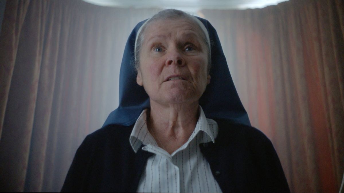 amulet2020 3 | film.org.pl Elderly woman in a blue-naved nun's habit looks upward with a concerned expression.