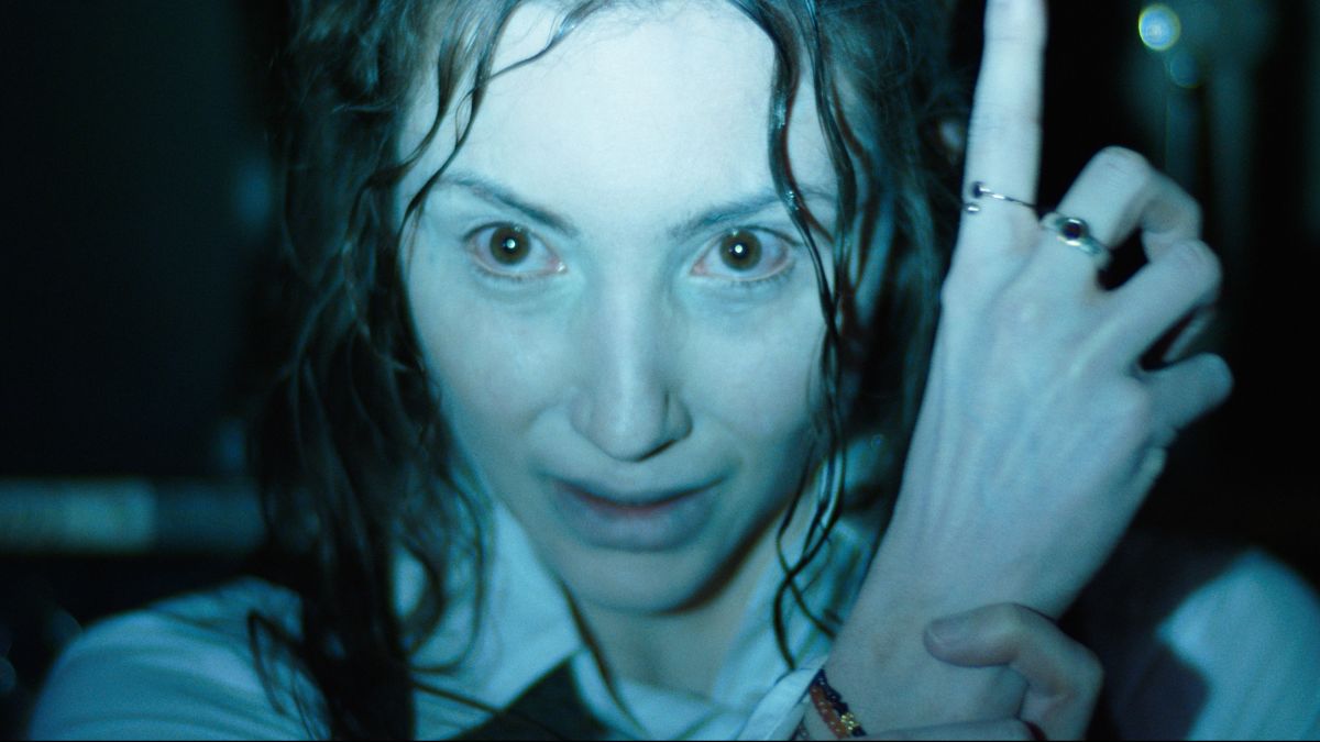 hokum2026 3 | film.org.pl Close-up of a woman with wet hair under blue lighting, her face close to the camera, hand with rings raised near her cheek.