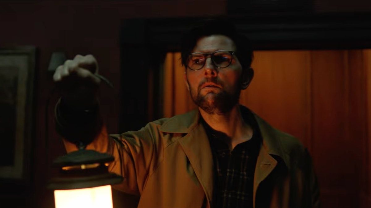 hokum2026 4 | film.org.pl Man wearing glasses and a brown coat holds a lit lantern in a dim, warm-lit room.