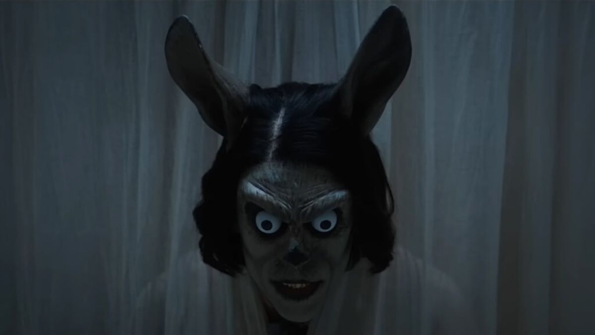 hokum2026 5 | film.org.pl Scary rabbit-faced figure with wide eyes peering through a white curtain.