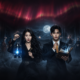 Two central figures—a woman with a blue lantern and a man with a glowing book—stand in a foggy, moonlit haunted room surrounded by ghostly figures.