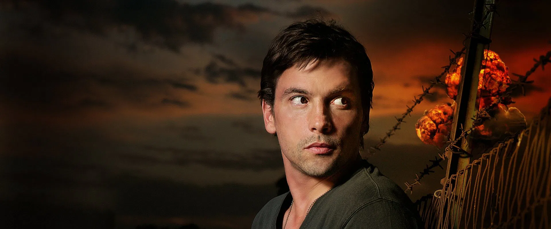 Portrait of a man looking to the right, with a barbed-wire fence and a fiery orange sunset in the background.