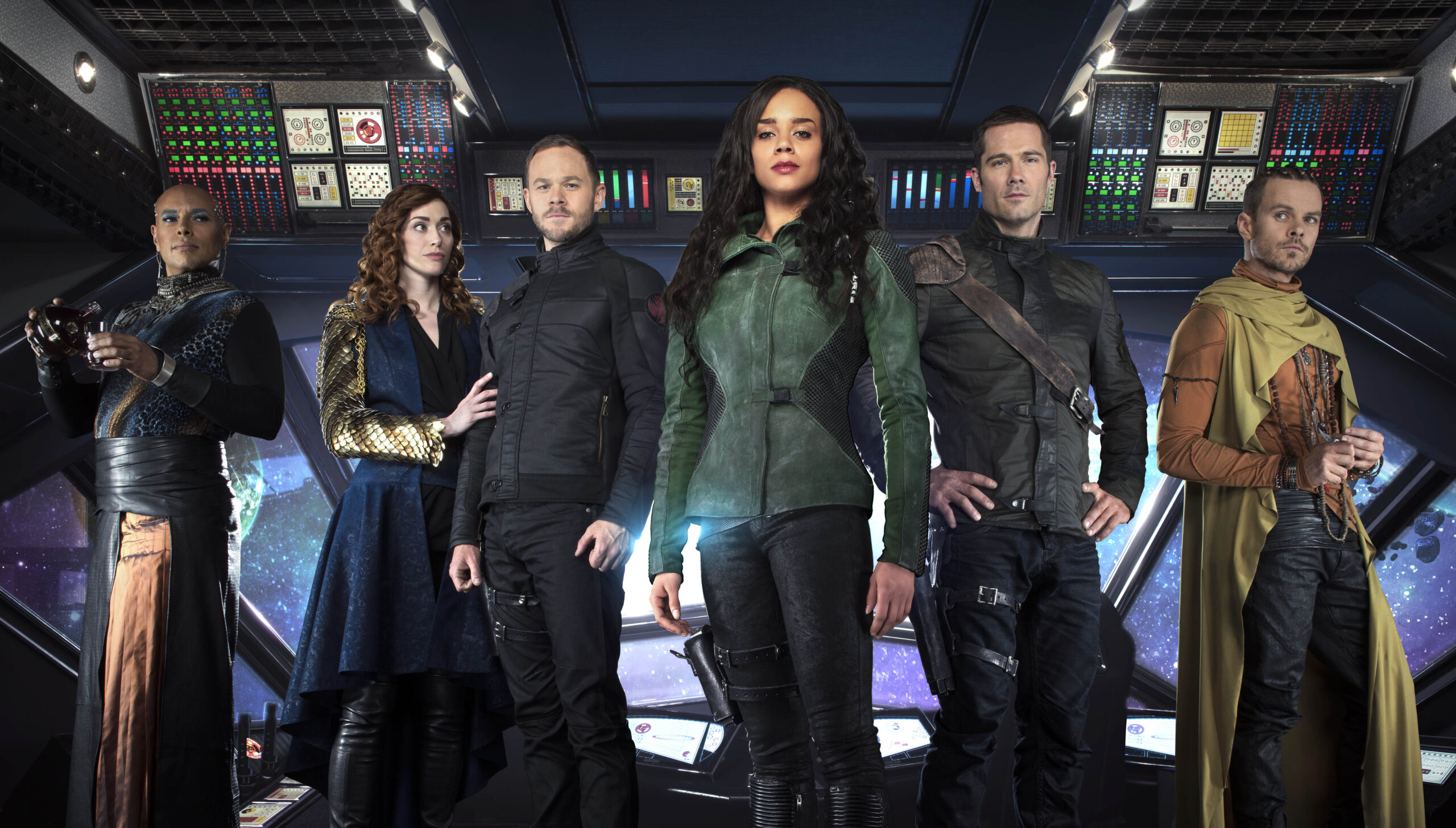 Six adults in sci‑fi costumes stand on a starship bridge, posing for the camera, with colorful control panels behind them.