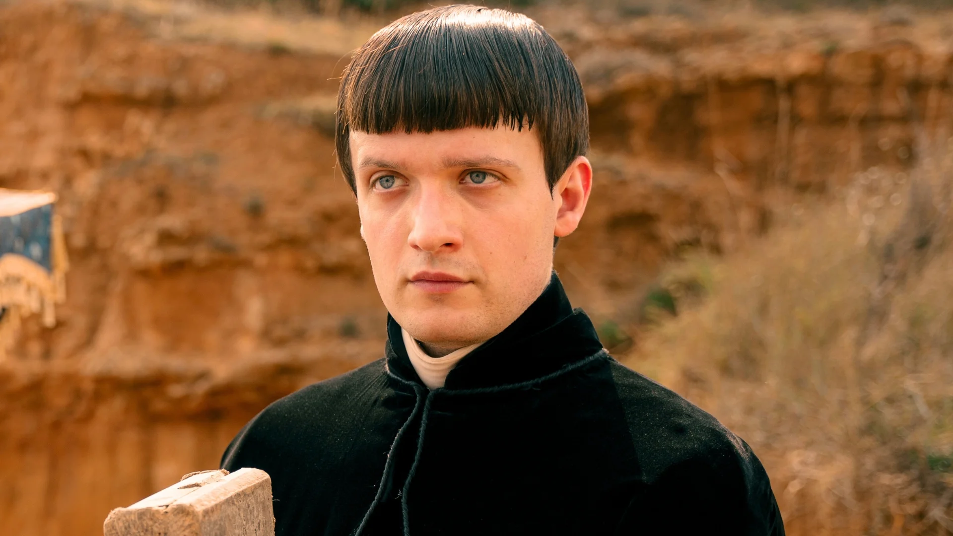 michal-sikorski-4 | film.org.pl Portrait of a man with a short black bowl haircut, wearing a black velvet cloak, outdoors in a warm-toned setting.
