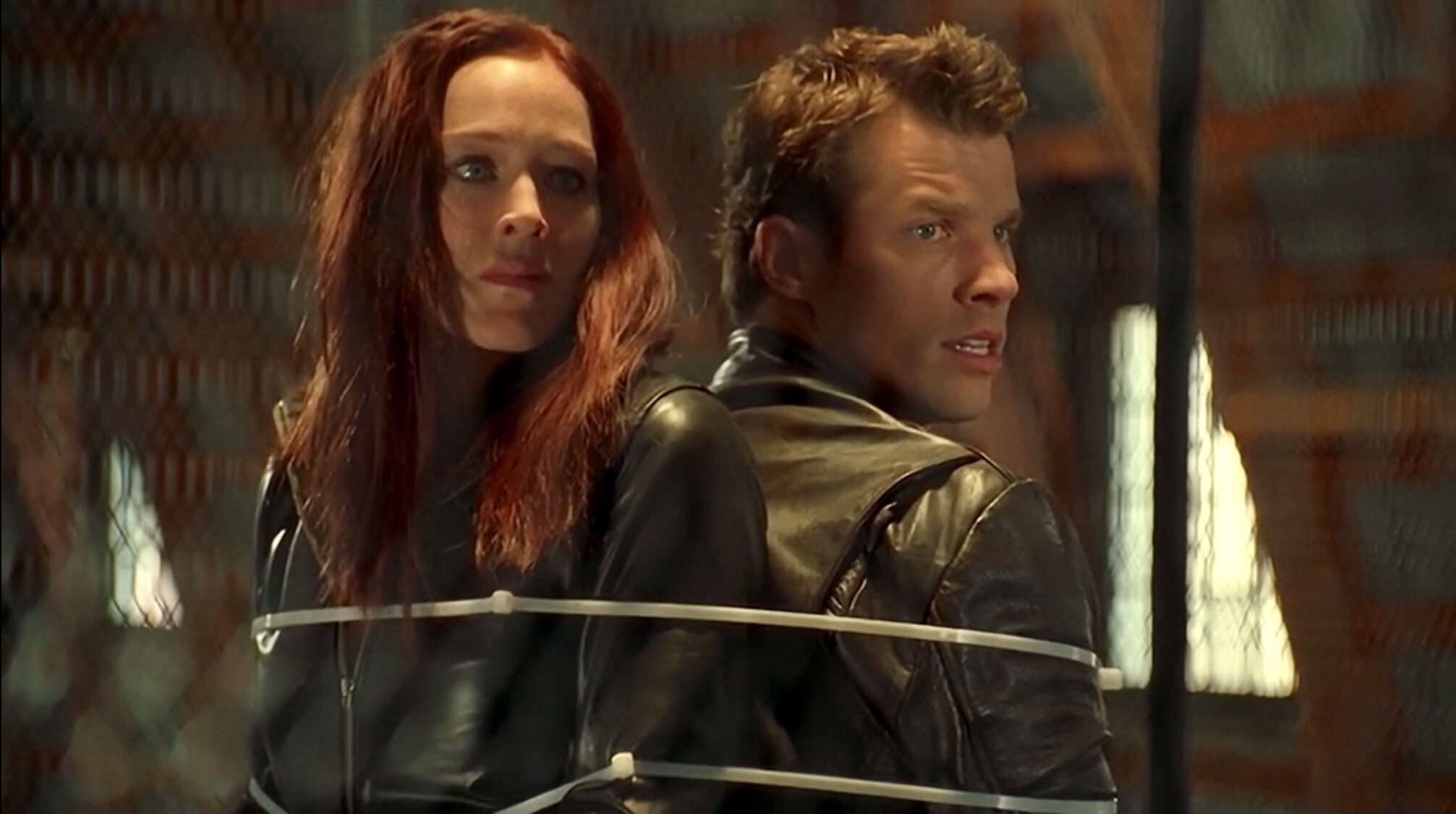 mutant-x-pokolenie-mutantow | film.org.pl Two people in leather jackets stand back-to-back, restrained with white zip ties, looking tense in a dim hallway.