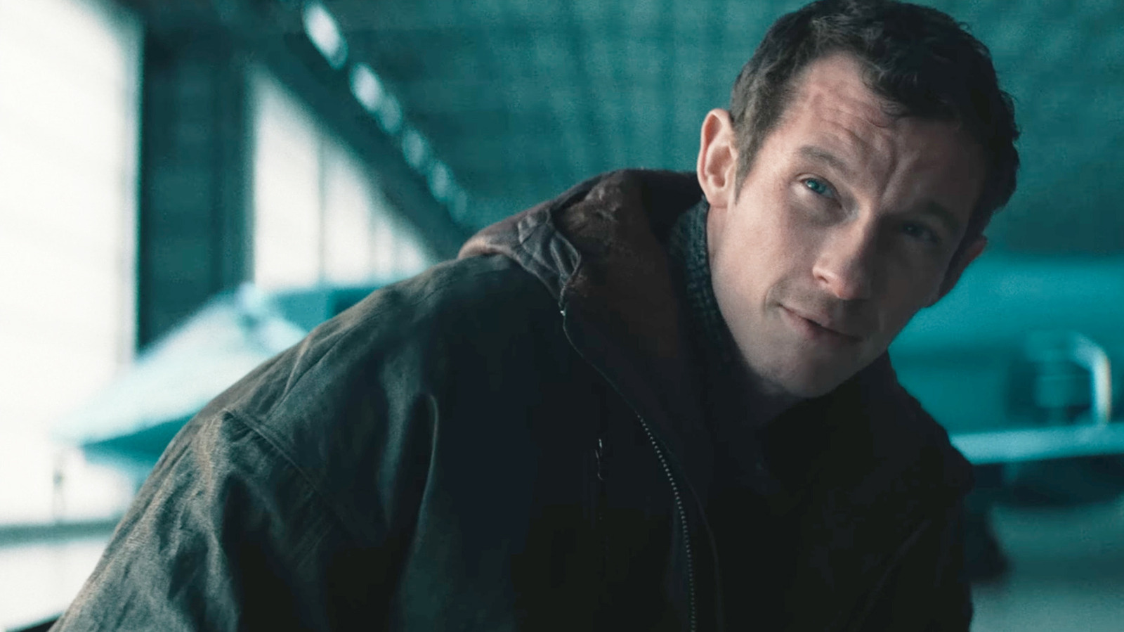 Neuromancer | film.org.pl Man in a dark jacket leans toward the camera with a faint smile in a blue-green, industrial-looking space.