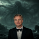 Man in a tuxedo stands before a dark, stormy seascape with a colossal tentacled monster looming behind him.