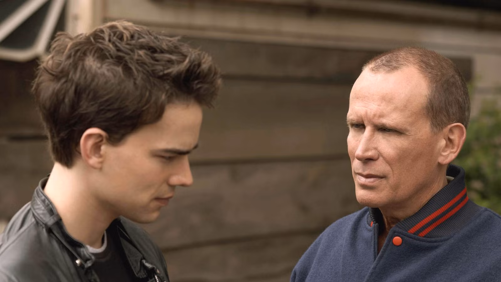 Two men are standing outdoors in a serious conversation, facing each other.