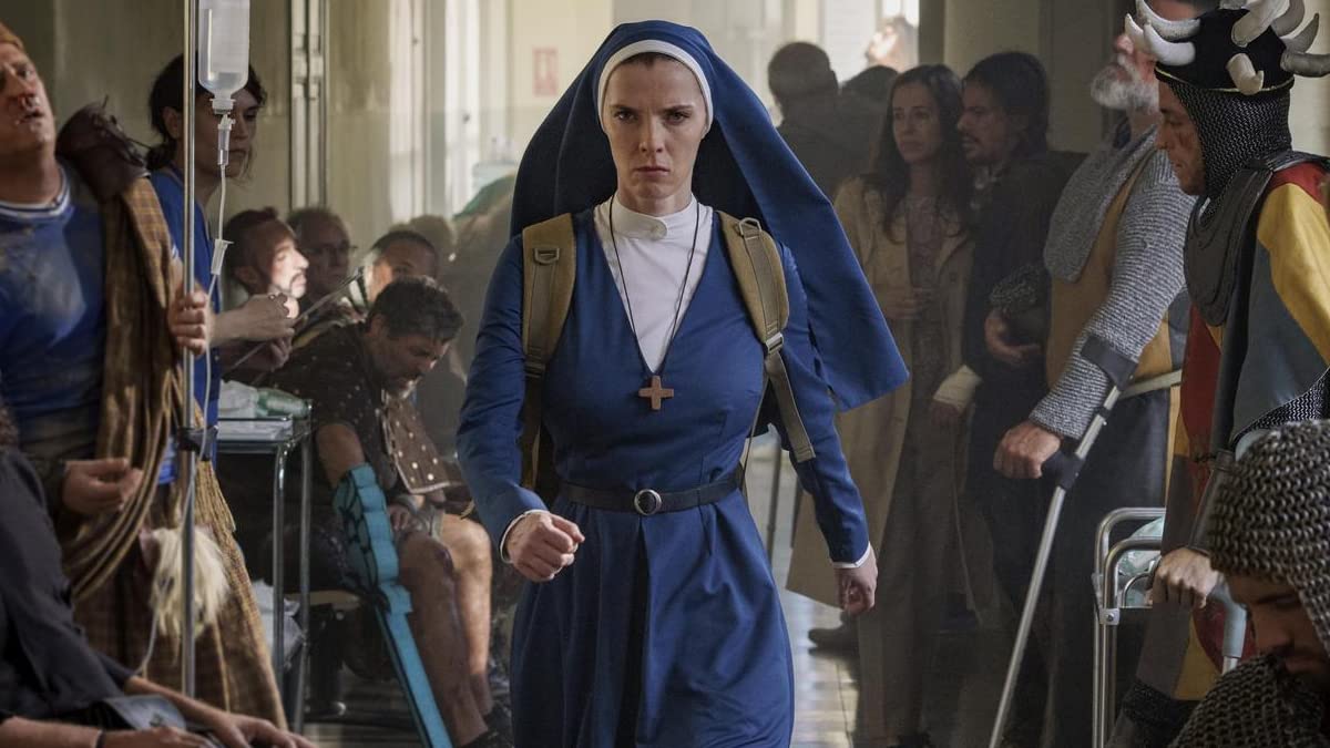 pani-davis-mrs-davis | film.org.pl A nun in a blue habit with a cross necklace walks down a hospital-like corridor among seated people and guards in medieval armor, looking determined.