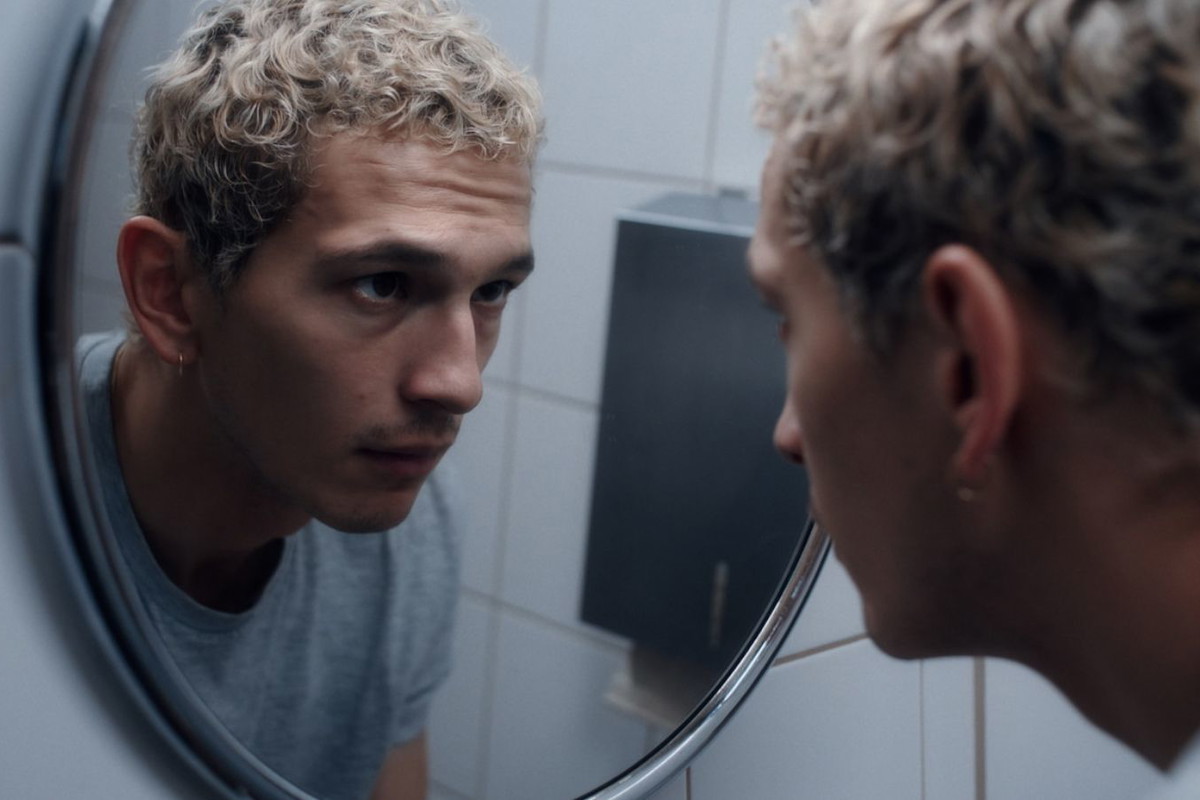 proud-10 | film.org.pl Young man in a gray shirt gazing at his reflection in a round bathroom mirror.