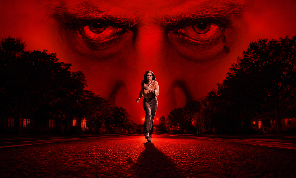 Woman runs toward the camera on a quiet suburban street; a giant red-tinted face with piercing eyes looms behind.
