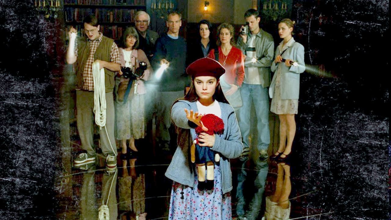 rose-red | film.org.pl Girl in a blue cardigan and red beret extends her hand toward the camera; a row of adults with cameras stands behind her in a dim room.