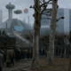 Man in a tan trench coat points as a crowd gathers in a dystopian urban scene with a neon Logan's Run sign and a Soylent Green truck in the foreground; ominous atmosphere.