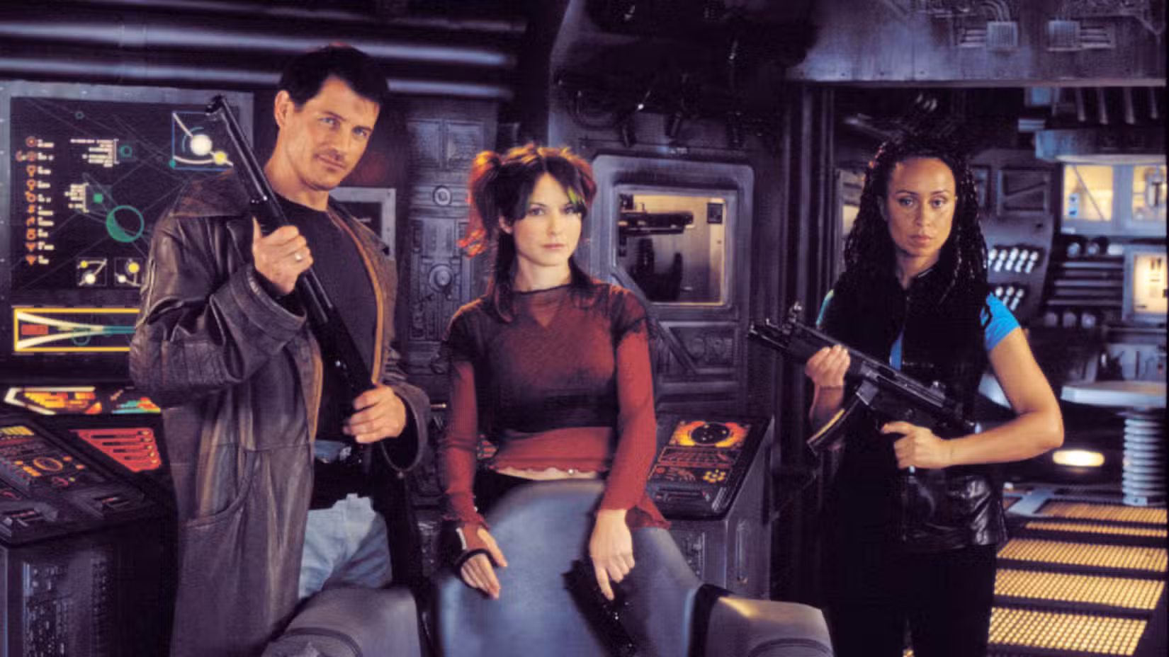 Three people in a futuristic control room pose with rifles, standing beside glowing dashboards and panels of a spaceship cockpit.