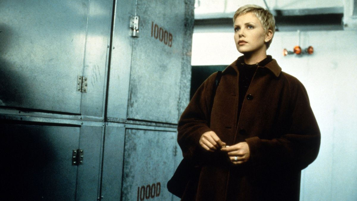 the-astronauts-wife-zona-astronauty | film.org.pl Woman with short blonde hair wearing a brown coat stands in a metal locker room, looking off to the side.
