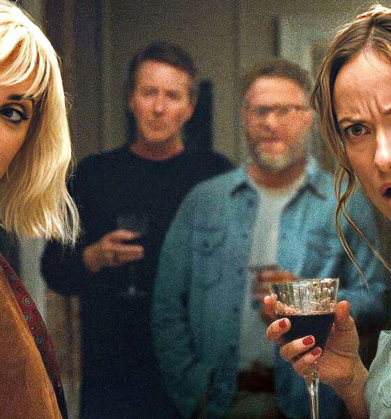 Two women at a party, facing the camera and holding drinks, with two men blurred in the background.