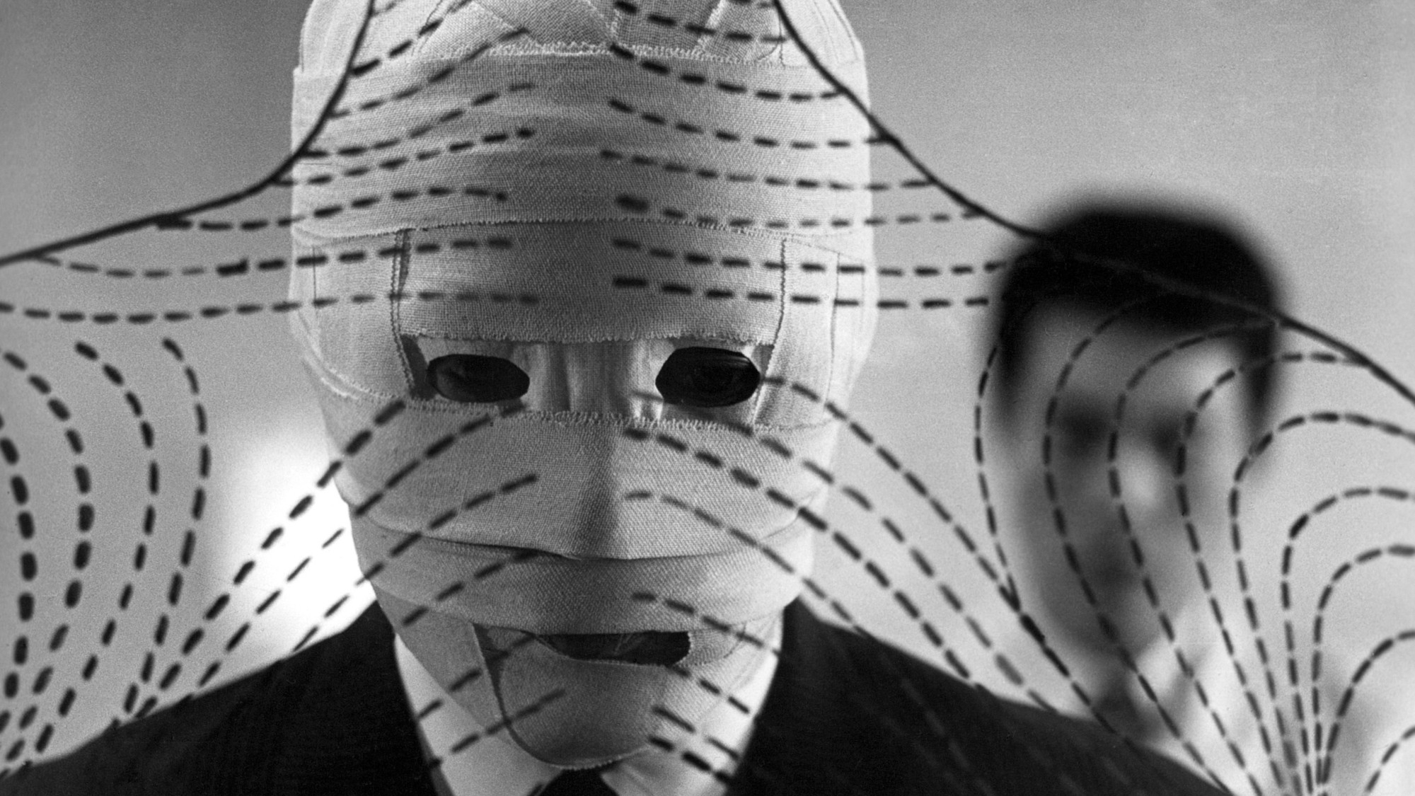 Person in a suit wrapped in bandage-like fabric with dashed tape patterns, grayscale, suggesting anonymity or concealment.