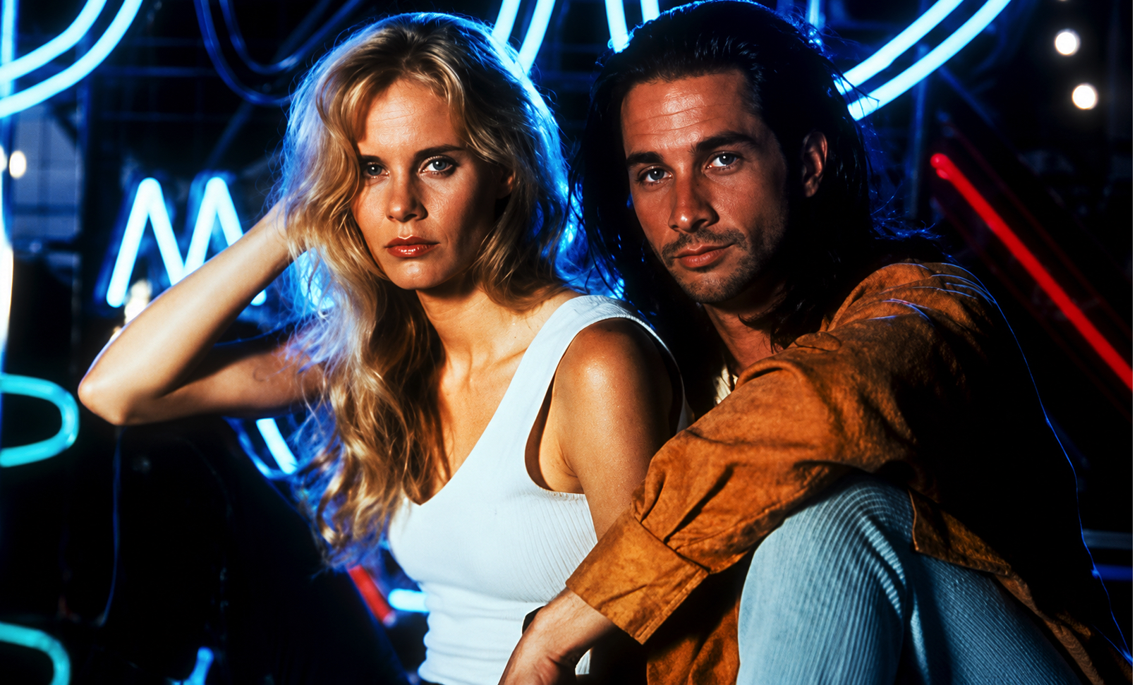 Blonde woman in a white tank top and a man with long dark hair pose close together in a neon blue-and-red club scene.