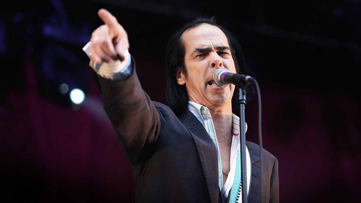 Male singer in a suit performing on stage, pointing toward the audience while singing into a microphone.